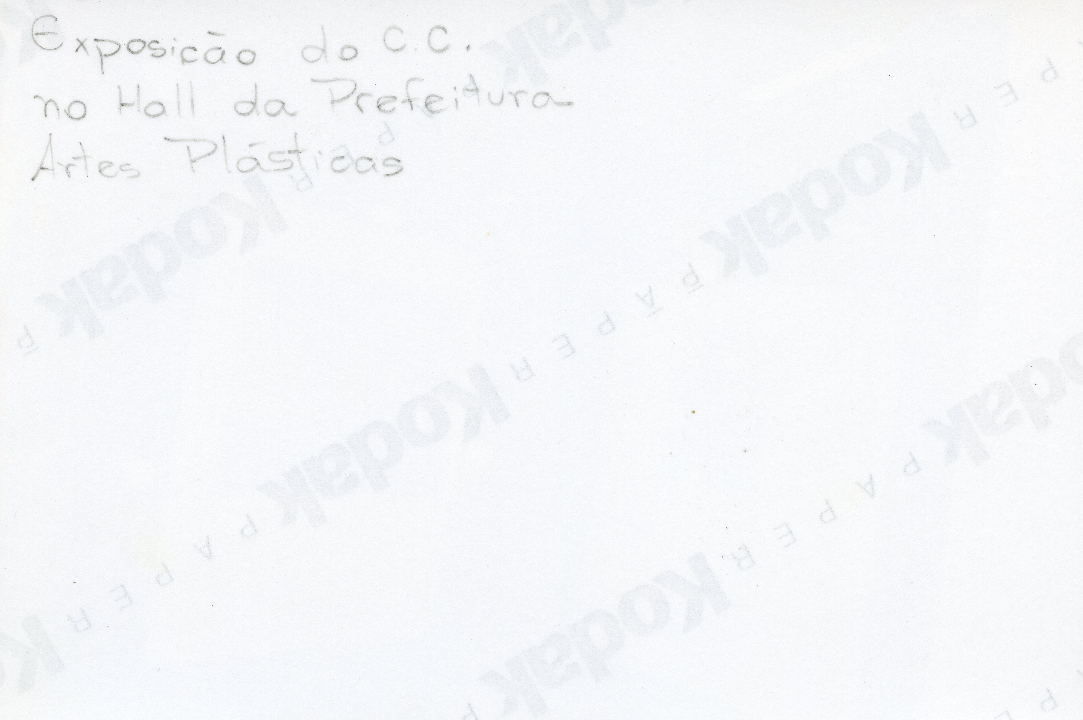 O verso de uma fotografia Kodak contendo uma anotação manuscrita a lápis sobre uma exposição de artes plásticas realizada no hall da prefeitura. O texto sugere um registro documental de um evento cultural local, possivelmente ocorrido na segunda metade do século XX.
