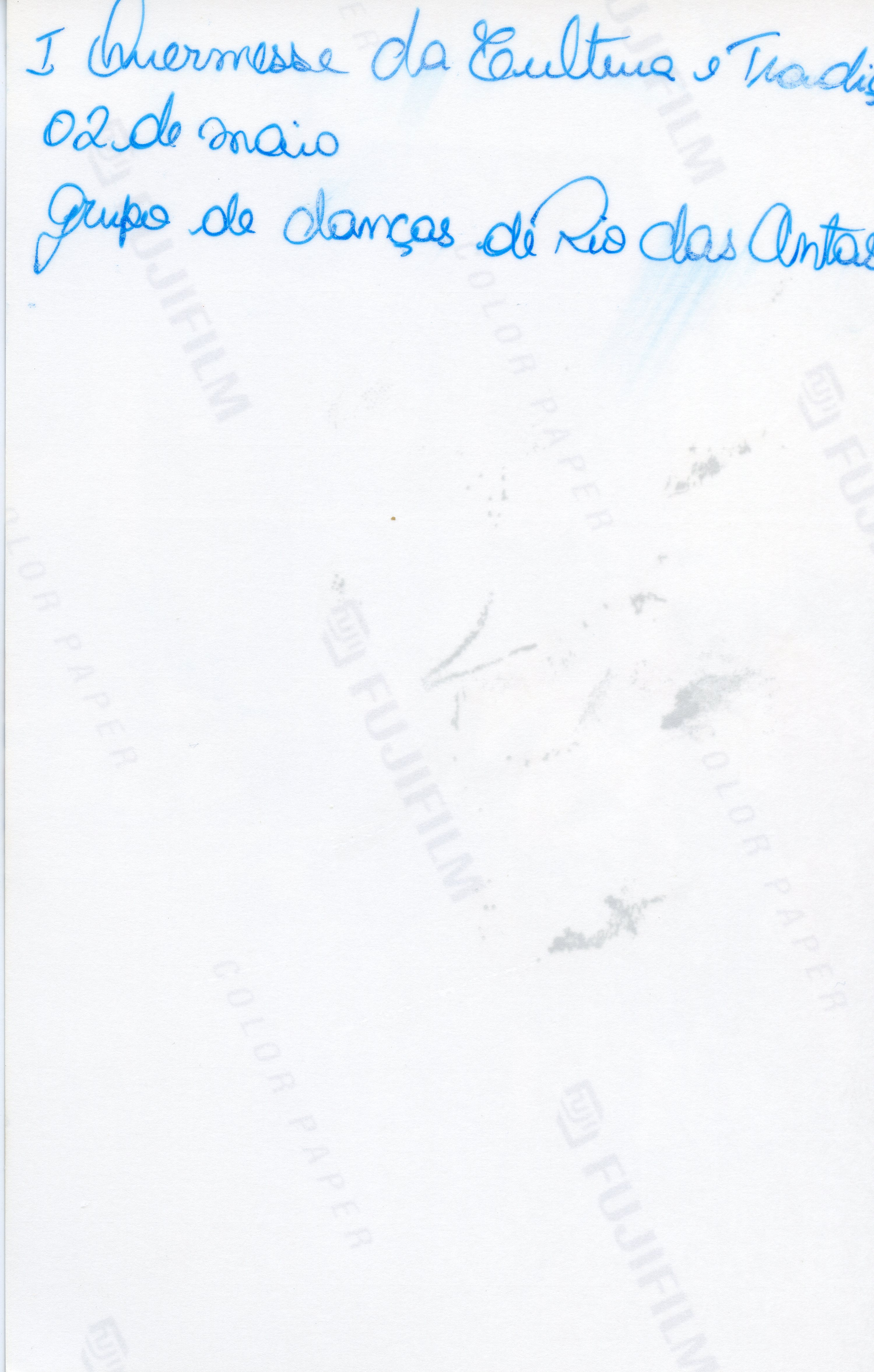 O verso de uma fotografia com anotações manuscritas em tinta azul, identificando um evento cultural. O texto menciona a 'I Quermesse da Cultura e Tradição' realizada em 2 de maio, envolvendo o grupo de danças de Rio das Antas.