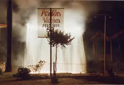 Uma fotografia noturna capturando uma queima de fogos em cascata, possivelmente uma homenagem comemorativa em Videira. O cartaz exibe a mensagem 'Parabéns Videira pelo seus 52 anos', indicando um evento de aniversário da cidade em um ambiente urbano ou de praça.