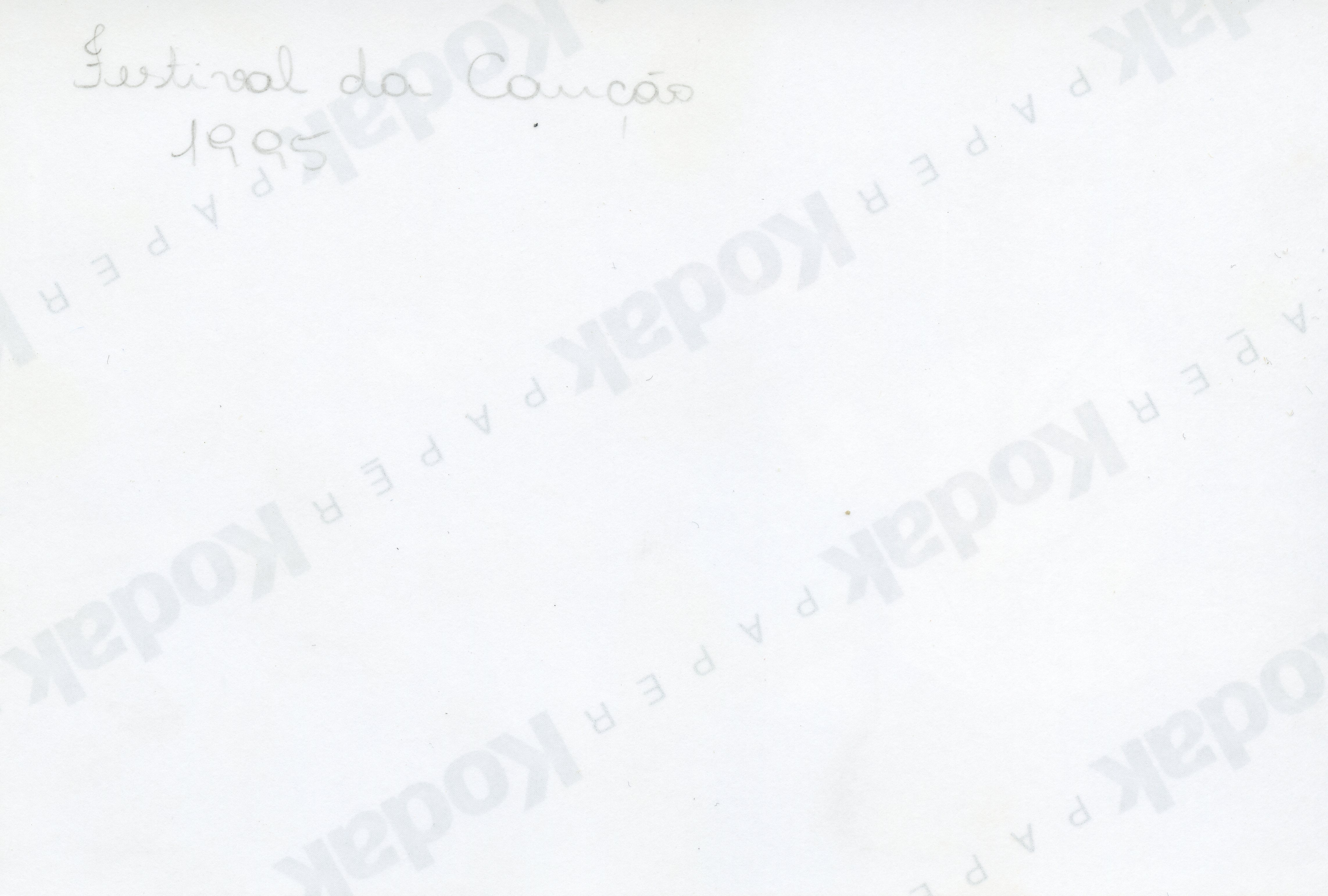 O verso de uma fotografia revelada em papel Kodak, contendo uma inscrição manuscrita a lápis que identifica o evento como 'Festival da Canção' e o ano de 1995. A marca d'água do fabricante do papel é visível na diagonal, indicando um registro fotográfico comum de eventos sociais ou culturais da época.