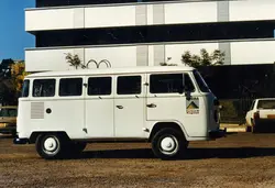 Uma fotografia lateral de uma Volkswagen Kombi branca estacionada em um terreno de terra batida, possivelmente em Videira, Santa Catarina. O veículo apresenta um adesivo oficial da prefeitura local com o slogan 'Certeza de Progresso', indicando uso institucional em um contexto de administração pública municipal, provavelmente entre as décadas de 1980 e 1990.