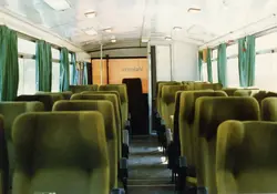 Interior de um ônibus de viagem antigo, apresentando poltronas estofadas em tom esverdeado e cortinas da mesma cor. Ao fundo, é possível ler a palavra 'Videira' em uma divisória, sugerindo uma conexão com a cidade catarinense, possivelmente em um veículo de transporte intermunicipal das décadas de 1970 ou 1980.