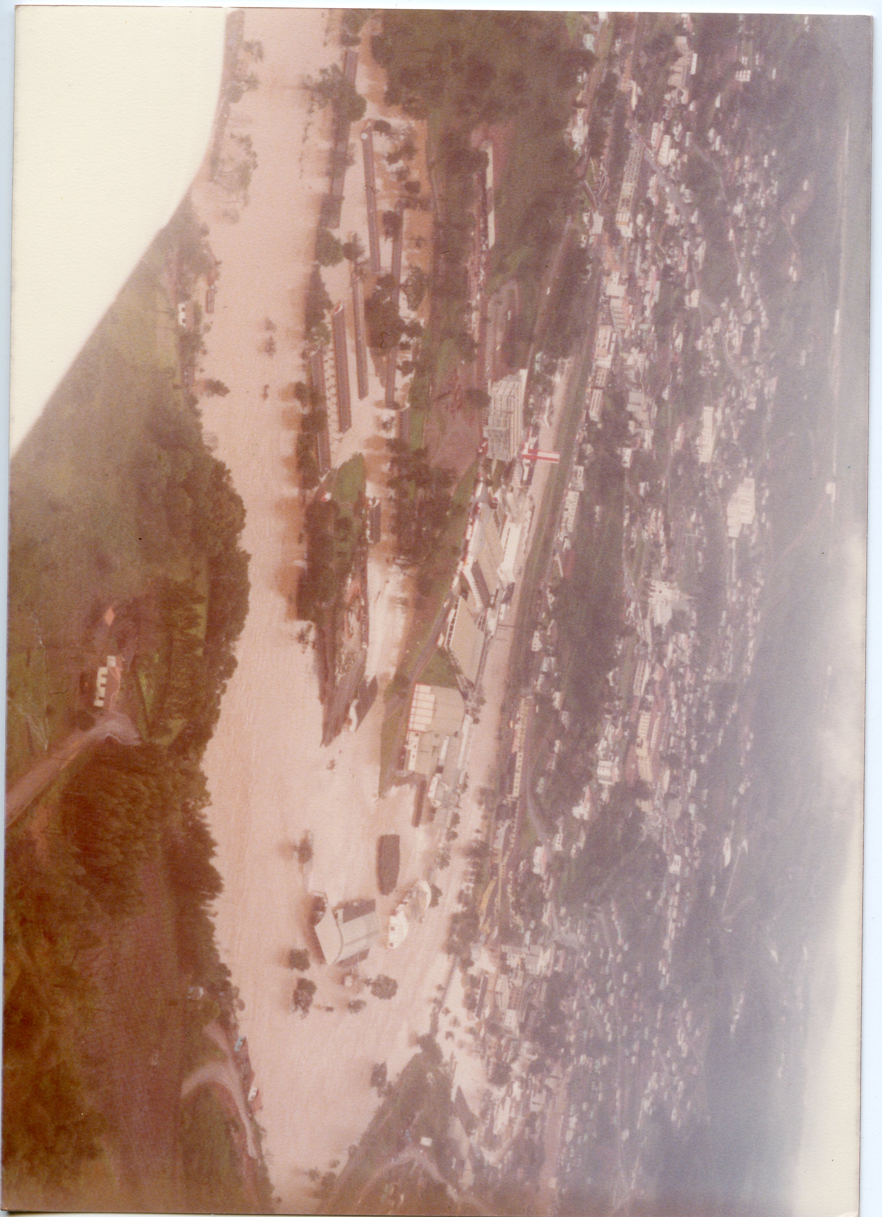 Fotografia aérea de uma enchente em uma área urbana, possivelmente em uma cidade do interior catarinense como Videira. A imagem mostra o rio transbordado cobrindo partes da infraestrutura urbana e industrial, com coloração barrenta característica de cheias.