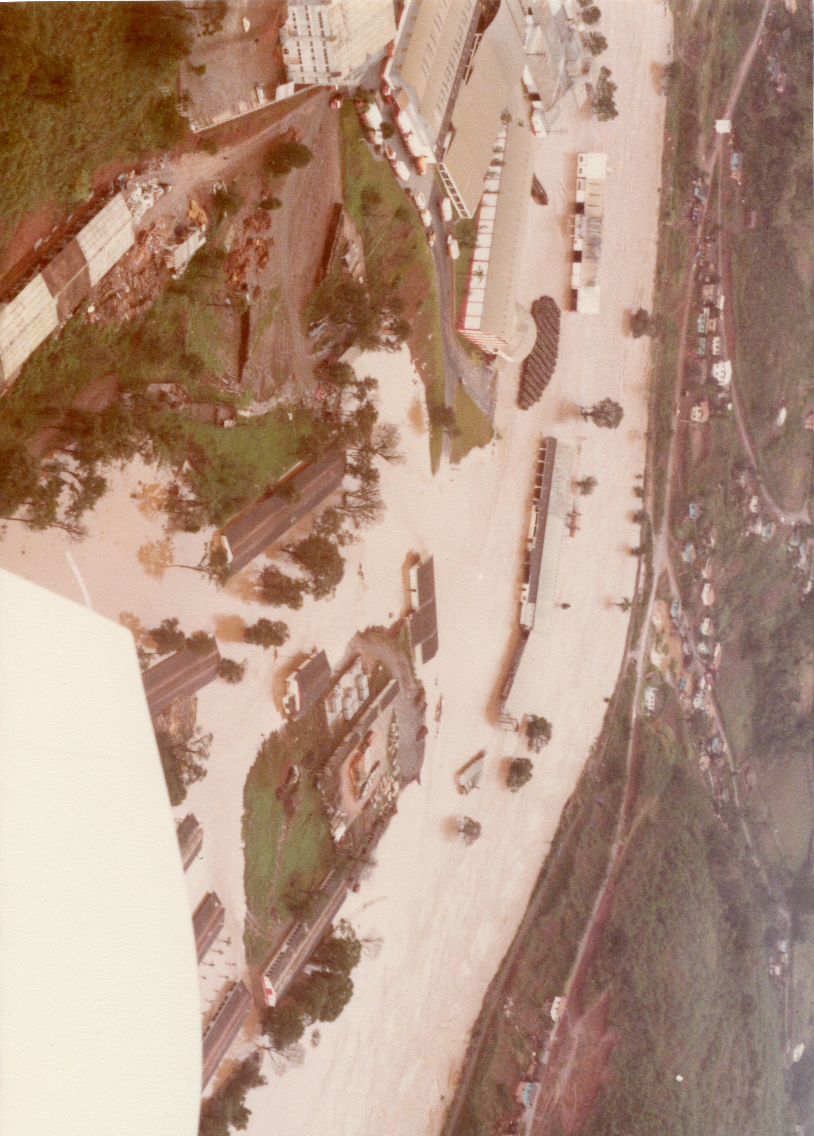 Vista aérea de uma área industrial ou urbana afetada por uma enchente severa, com águas barrentas cobrindo grande parte do terreno e cercando construções. A imagem, provavelmente da segunda metade do século XX, mostra galpões e infraestrutura logística submersos, sugerindo um evento climático de grande impacto em uma região brasileira.