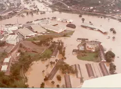 Uma vista aérea de uma enchente severa em uma área industrial e urbana, possivelmente em Videira, Santa Catarina. A imagem mostra galpões e estruturas parcialmente submersos por águas barrentas, sugerindo um evento climático significativo ocorrido provavelmente nas décadas de 1980 ou 1990.