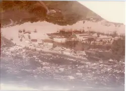 Fotografia aérea mostrando uma enchente severa que inunda áreas urbanas e industriais próximas a um rio. A imagem registra um evento climático significativo, possivelmente em uma cidade do interior catarinense, com construções parcialmente submersas e sedimentos visíveis na água.