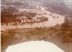 Vista aérea de uma enchente severa em uma área urbana e industrial, possivelmente em uma cidade do interior catarinense como Videira. A imagem mostra o rio transbordado cobrindo grande parte das construções e infraestrutura, com coloração sépia típica de fotografias das décadas de 1970 ou 1980.