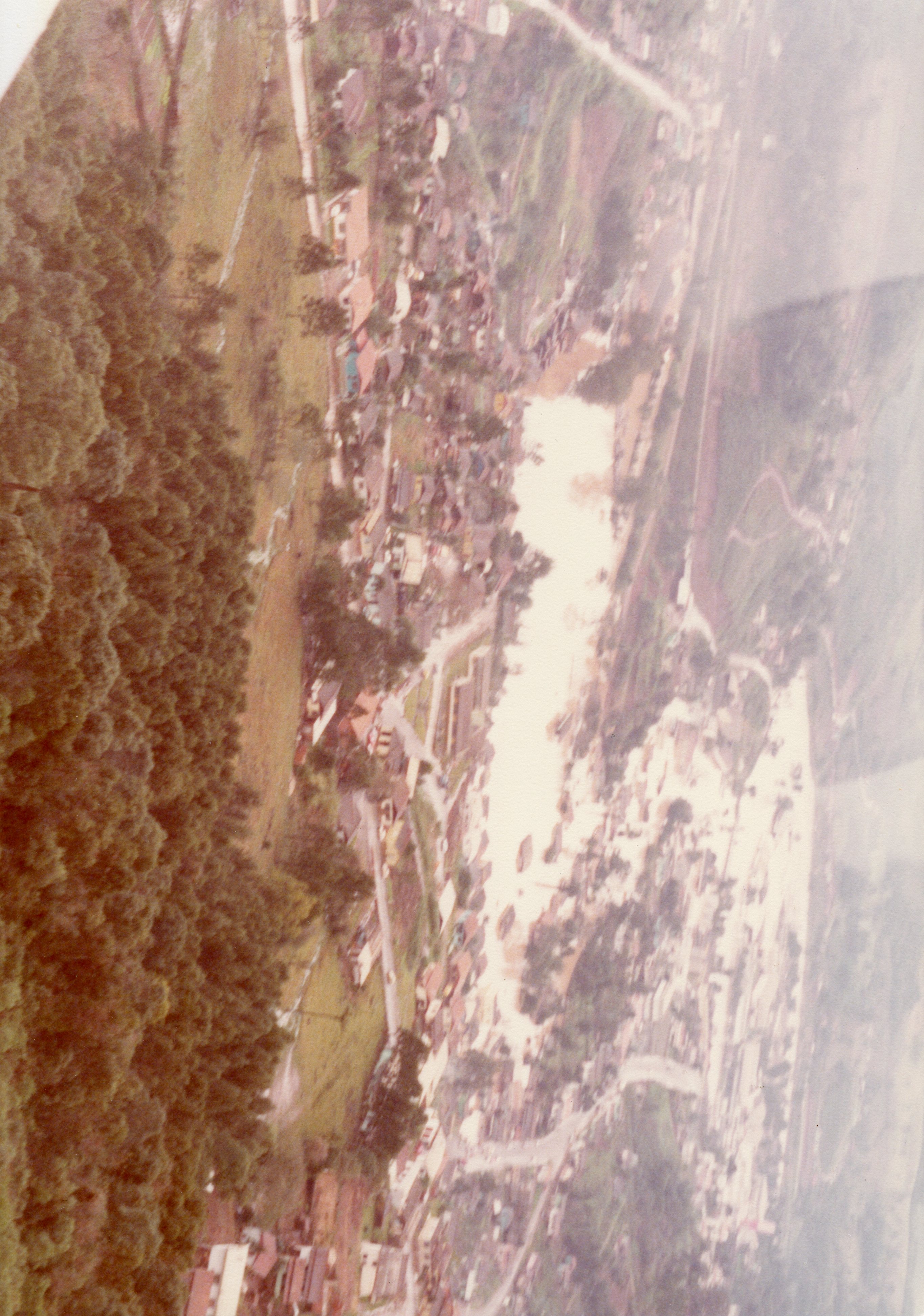 Uma vista aérea de uma pequena cidade brasileira, possivelmente em uma região de colonização com relevo acidentado e vegetação densa. A imagem apresenta tons sépia, sugerindo uma fotografia de meados do século XX, capturando o traçado urbano inicial e a ocupação do solo em torno de uma área central.