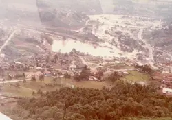 Uma vista aérea de uma pequena cidade brasileira, possivelmente em uma região de colonização com relevo acidentado e vegetação densa. A imagem apresenta tons sépia, sugerindo uma fotografia de meados do século XX, capturando o traçado urbano inicial e a ocupação do solo em torno de uma área central.