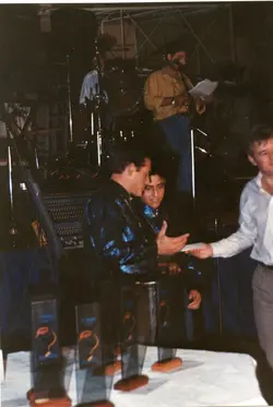 Uma fotografia de um evento social ou premiação em ambiente interno, possivelmente um salão de festas ou clube. Vê-se homens entregando ou recebendo documentos/prêmios, com uma banda musical ao fundo, sugerindo uma cerimônia de homenagem ou evento corporativo típico da década de 1990.