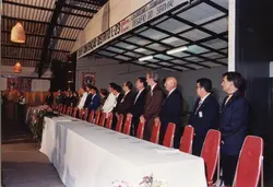 Uma fotografia de um evento formal do Lions Clube, possivelmente uma convenção distrital, com várias pessoas sentadas à mesa em um salão. O ambiente apresenta decoração com faixas e estandartes do Lions, sugerindo um encontro de lideranças ou membros da organização em um contexto comunitário brasileiro.