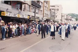 Uma fotografia de um desfile ou evento público em uma rua urbana, possivelmente em uma cidade brasileira como Videira, com uma multidão de pessoas caminhando e segurando balões. A arquitetura dos prédios ao fundo e as vestimentas sugerem um cenário urbano típico do final do século XX, provavelmente entre as décadas de 1980 e 1990.