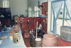 Uma exposição interna que retrata a cultura rural e a produção artesanal, possivelmente em um museu ou centro cultural de uma cidade como Videira. O ambiente apresenta diversos utensílios antigos, como barris de madeira, garrafões de vinho, ferramentas agrícolas e objetos domésticos, evocando a história da colonização e da vitivinicultura na região.