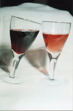 Uma fotografia de duas taças de cristal com detalhes lapidados, contendo vinhos de diferentes tonalidades, realizando um brinde. A imagem evoca um momento de celebração, possivelmente associado à cultura vitivinícola de regiões como Videira, em um contexto social ou de degustação.