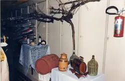 Uma exibição temática relacionada à vitivinicultura, contendo barris de madeira, garrafões revestidos e uma videira seca, possivelmente em um evento cultural ou comercial. A cena remete à tradição da produção de vinho, comum em regiões de colonização italiana como Videira, com elementos decorativos dispostos sobre uma mesa.