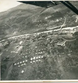 Fotografia aérea em preto e branco de uma pequena cidade brasileira, possivelmente em fase de expansão urbana inicial. A imagem revela um traçado urbano com casas dispostas de forma organizada, um rio atravessando a paisagem e áreas de vegetação nativa ao redor, sugerindo um contexto de colonização ou desenvolvimento regional do século XX.