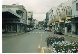 Uma vista de rua urbana em uma cidade brasileira, possivelmente Videira, caracterizada por arquitetura comercial com marquises metálicas arqueadas e lojas de departamentos. A presença de veículos como um Volkswagen Fusca e modelos dos anos 90 sugere que a fotografia foi tirada no final do século XX, provavelmente entre as décadas de 1990 e 2000.