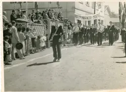 Fotografia em preto e branco de um desfile cívico, provavelmente em comemoração ao 7 de setembro, em uma pequena cidade brasileira. Observa-se um grupo de jovens marchando com uma faixa onde se lê 'Independência ou Morte', enquanto espectadores acompanham o evento atrás de uma cerca de madeira.