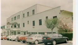 Fotografia externa do Hospital Santa Maria, exibindo uma arquitetura funcionalista de meados do século XX. A cena mostra uma fileira de veículos estacionados em frente à fachada do edifício, sugerindo um registro cotidiano de uma cidade brasileira de médio porte.