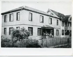 Fotografia em preto e branco de um casarão de dois andares com arquitetura típica de colonização europeia, possivelmente no sul do Brasil. Observa-se um grupo de pessoas sentado na varanda frontal, protegida por uma cerca de madeira, sugerindo um ambiente residencial ou institucional do início do século XX.