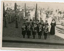 Fotografia em preto e branco de um desfile cívico ou religioso, provavelmente em meados do século XX, mostrando crianças segurando letras que formam a palavra 'BRASIL SALVE'. O grupo é acompanhado por jovens uniformizados e uma freira, em um ambiente externo com calçamento de paralelepípedos, sugerindo uma celebração escolar ou comunitária em uma cidade brasileira.