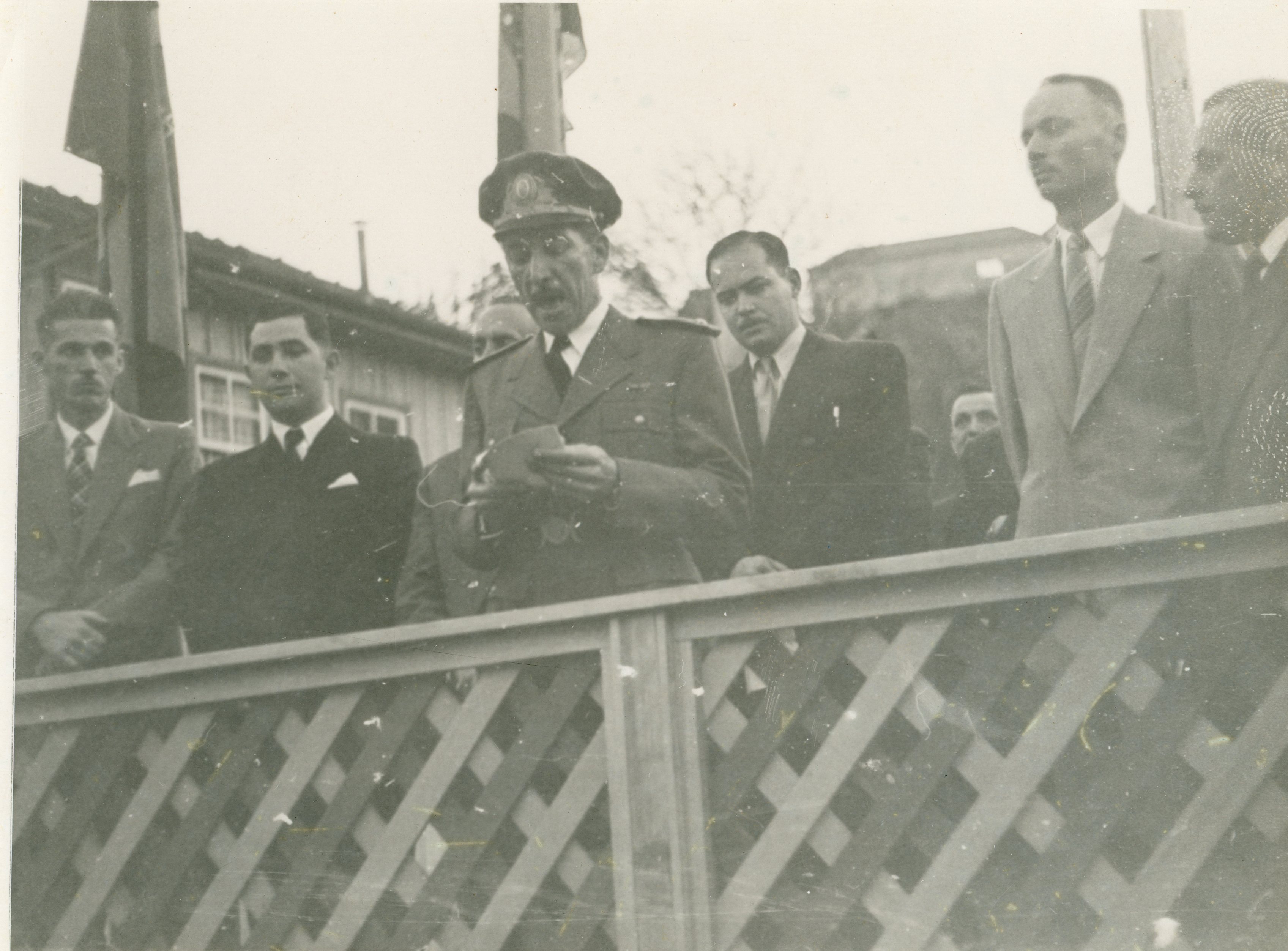 Fotografia em preto e branco retratando um oficial militar discursando em um evento público, possivelmente uma cerimônia oficial em uma pequena cidade brasileira. O grupo de homens ao redor veste trajes formais da época, sugerindo um contexto político ou cívico ocorrido em meados do século XX.