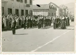 Fotografia histórica em preto e branco retratando um desfile cívico ou religioso em uma rua de terra, com crianças uniformizadas marchando e uma freira acompanhando o grupo. O cenário apresenta construções de madeira típicas da colonização sulista brasileira, sugerindo um ambiente urbano em desenvolvimento na primeira metade do século XX.