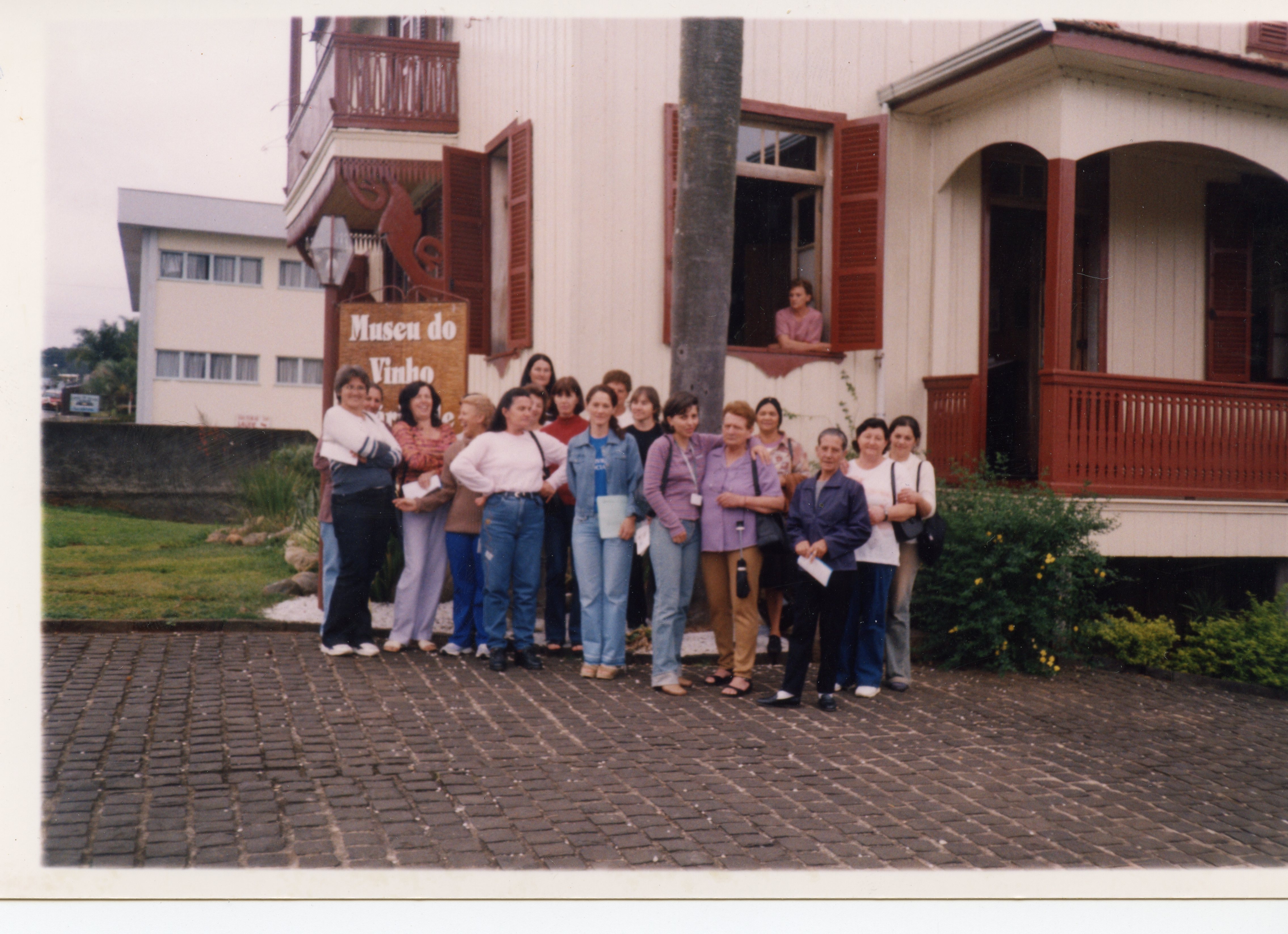 Um grupo de mulheres posa em frente ao Museu do Vinho, em uma construção de arquitetura colonial de madeira com detalhes em vermelho. A cena sugere uma visita turística ou evento cultural, provavelmente ocorrido no final do século XX, dado o estilo das vestimentas casuais.