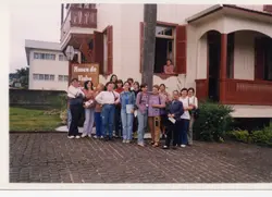 Um grupo de mulheres posa em frente ao Museu do Vinho, em uma construção de arquitetura colonial de madeira com detalhes em vermelho. A cena sugere uma visita turística ou evento cultural, provavelmente ocorrido no final do século XX, dado o estilo das vestimentas casuais.