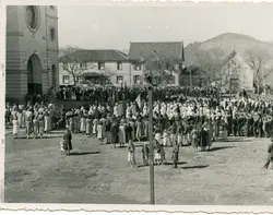 Uma fotografia em preto e branco que registra uma grande procissão ou evento religioso em frente a uma igreja de arquitetura clássica. A cena mostra uma multidão, incluindo muitas mulheres vestidas com roupas formais da época, sugerindo um contexto de colonização ou vida comunitária no interior do Brasil em meados do século XX.