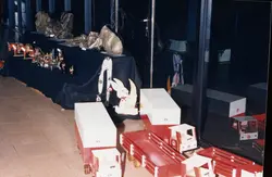 Uma fotografia que mostra uma vitrine ou exposição interna contendo brinquedos de madeira artesanais, incluindo trens e figuras decorativas como um coelho. A cena parece ser de uma exposição comercial ou escolar, possivelmente datada entre as décadas de 1980 e 1990, com elementos decorativos dispostos sobre um tecido escuro.