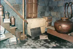 A imagem mostra uma exposição ou acervo de objetos históricos, possivelmente relacionados à agricultura ou produção artesanal, como alambiques de cobre e ferramentas de madeira. O cenário apresenta paredes de pedra rústica e prateleiras improvisadas, sugerindo um museu local ou uma adega antiga, comum em regiões de colonização europeia no sul do Brasil.