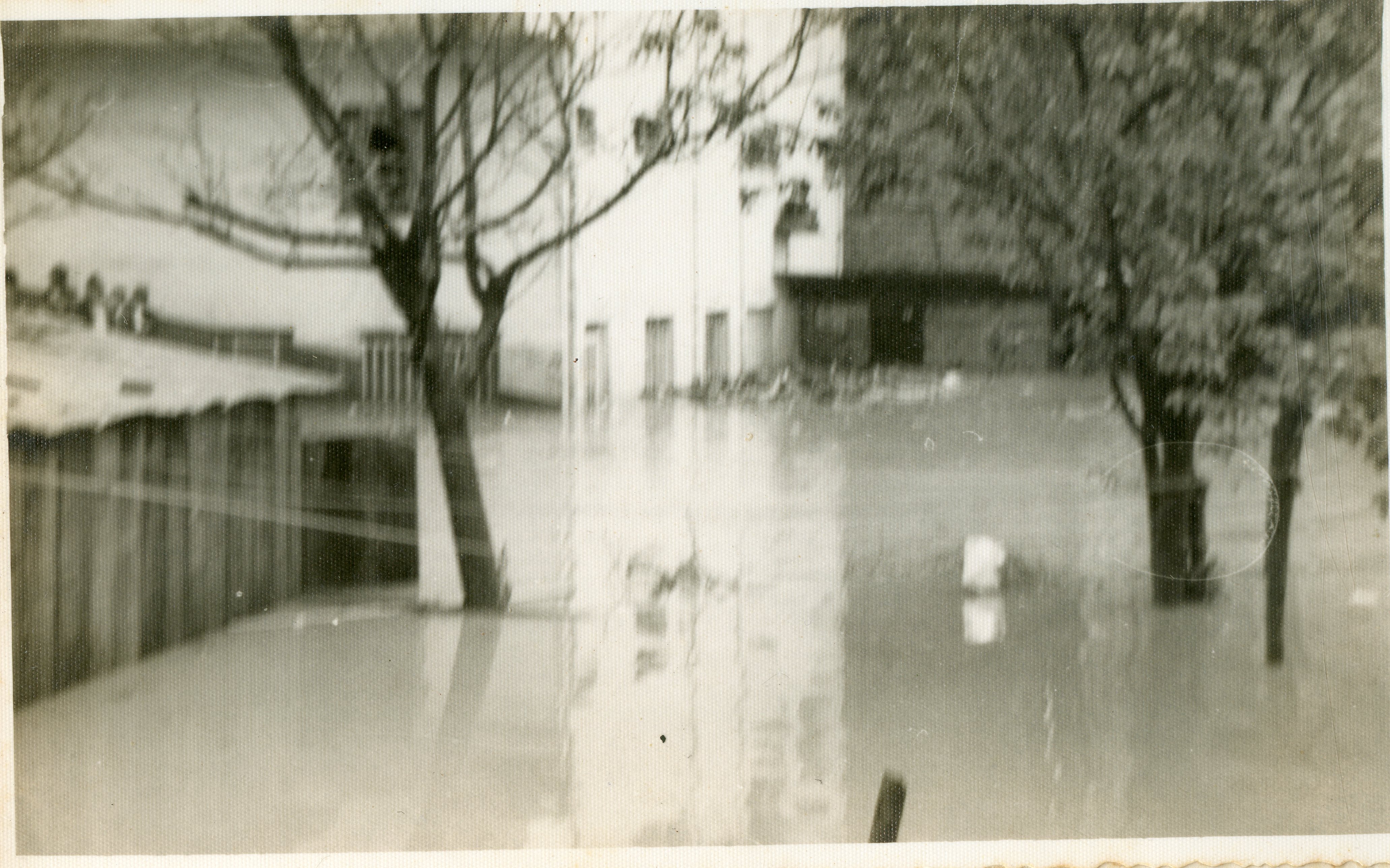 Fotografia em preto e branco que registra uma enchente urbana, com águas cobrindo a parte inferior de edificações e árvores. A imagem sugere um evento climático histórico em uma área residencial ou comercial, possivelmente em uma cidade do interior brasileiro, dada a arquitetura simples e a vegetação.