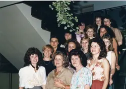 Uma fotografia de grupo composta por diversas mulheres posando em uma escadaria interna, provavelmente em um ambiente social ou de trabalho. O estilo dos penteados volumosos e das vestimentas sugere que a imagem foi capturada durante a década de 1980 ou início da década de 1990.