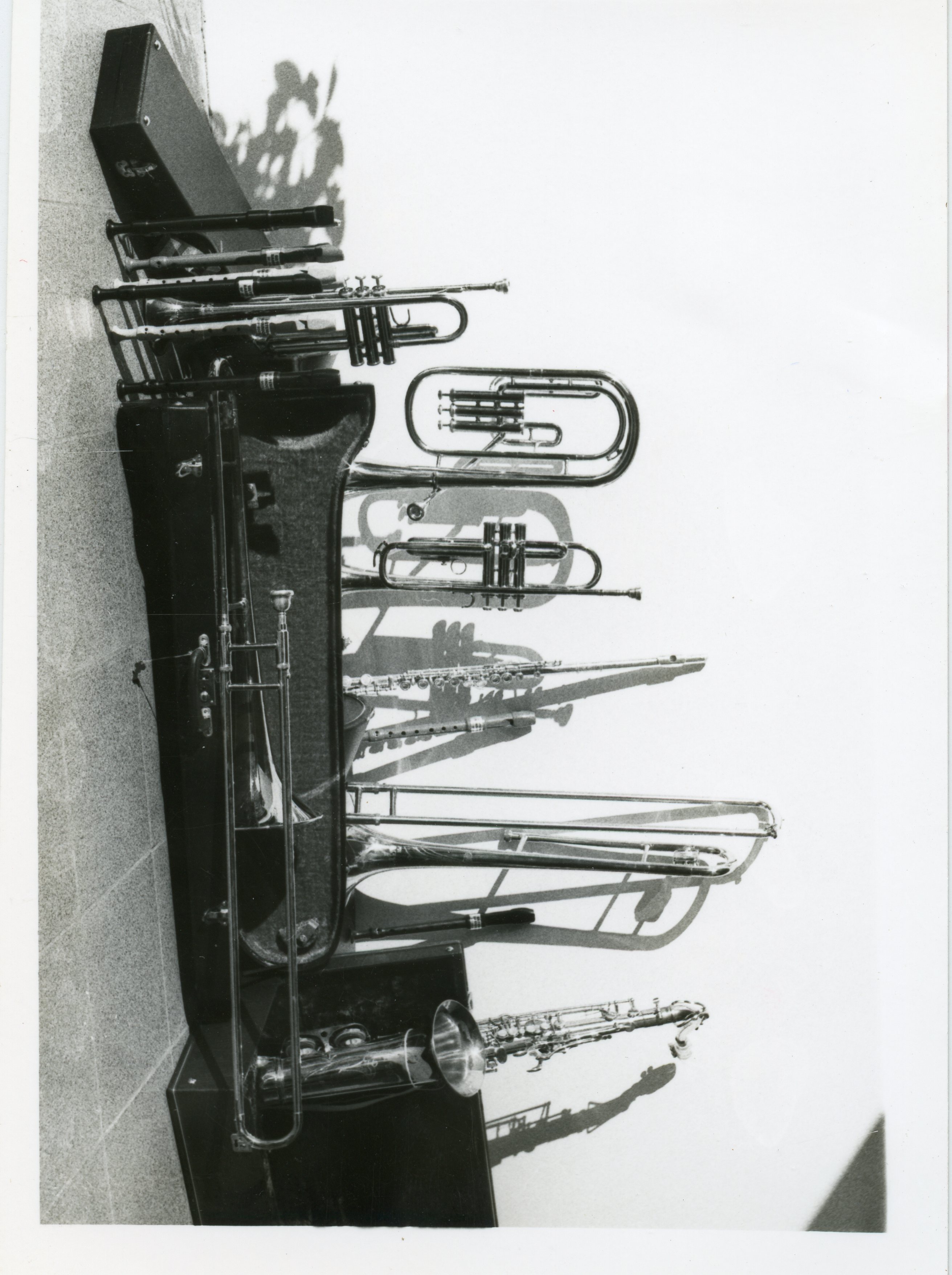 Uma fotografia em preto e branco exibindo uma coleção de instrumentos musicais de sopro, incluindo trompetes, trombones e um saxofone, dispostos sobre ou próximos a seus estojos. A imagem sugere um contexto de banda musical ou fanfarra, possivelmente em uma cidade pequena como Videira, com uma estética que remete à metade do século XX.