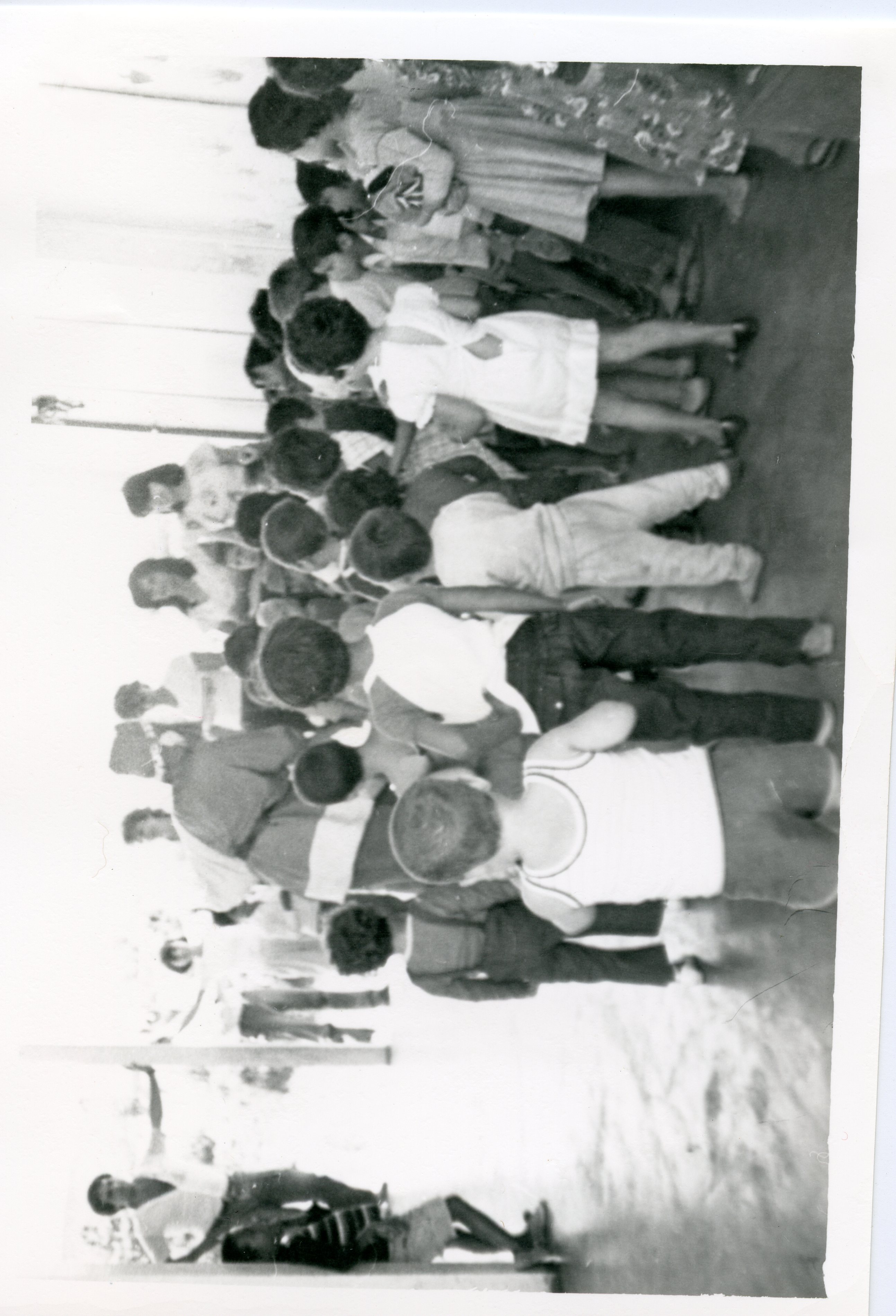 Fotografia em preto e branco capturando uma fila de crianças em um ambiente interno, possivelmente uma escola ou centro comunitário. As vestimentas e o estilo da imagem sugerem um contexto brasileiro de meados do século XX, possivelmente entre as décadas de 1960 e 1970.