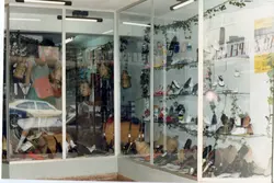 Uma fotografia de uma vitrine de loja, possivelmente uma sapataria ou comércio local, decorada com elementos rústicos como barris de madeira e cestos de vime. A imagem reflete o estilo de vitrinismo comercial de meados da década de 1990, com manequins e calçados expostos em prateleiras de vidro.