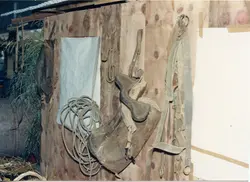 A imagem mostra uma parede de madeira rústica onde estão pendurados diversos arreios, selas e cordas de couro, típicos de atividades rurais e tropeiras. O cenário sugere um ambiente de galpão ou celeiro, possivelmente em uma região de colonização agrícola, refletindo costumes tradicionais do interior brasileiro.