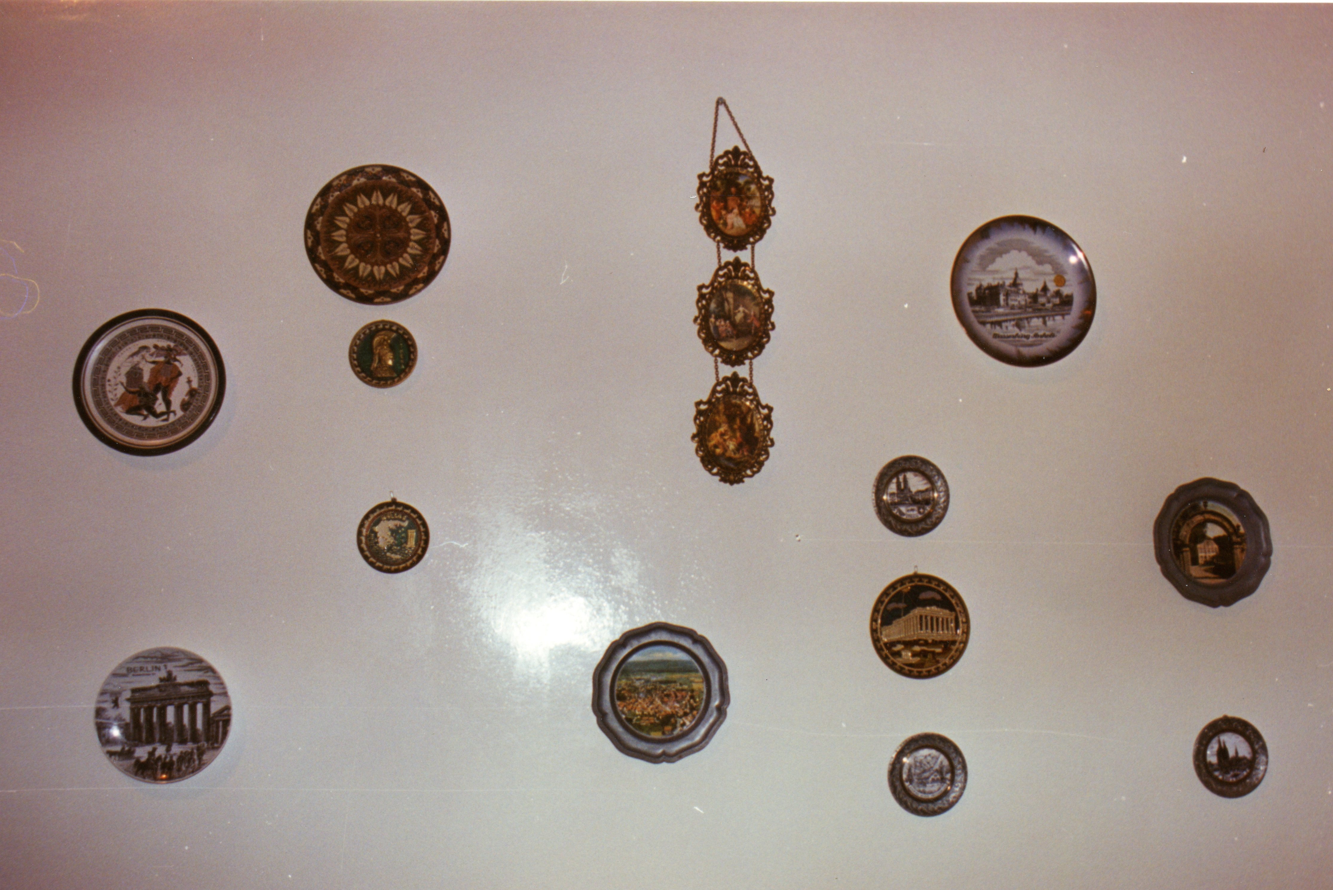 Uma parede decorada com diversos pratos ornamentais de diferentes tamanhos e formatos, exibindo imagens de paisagens e monumentos europeus. A disposição sugere uma coleção pessoal de lembranças de viagens, comum em residências brasileiras de meados do século XX.