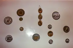 Uma parede decorada com diversos pratos ornamentais de diferentes tamanhos e formatos, exibindo imagens de paisagens e monumentos europeus. A disposição sugere uma coleção pessoal de lembranças de viagens, comum em residências brasileiras de meados do século XX.
